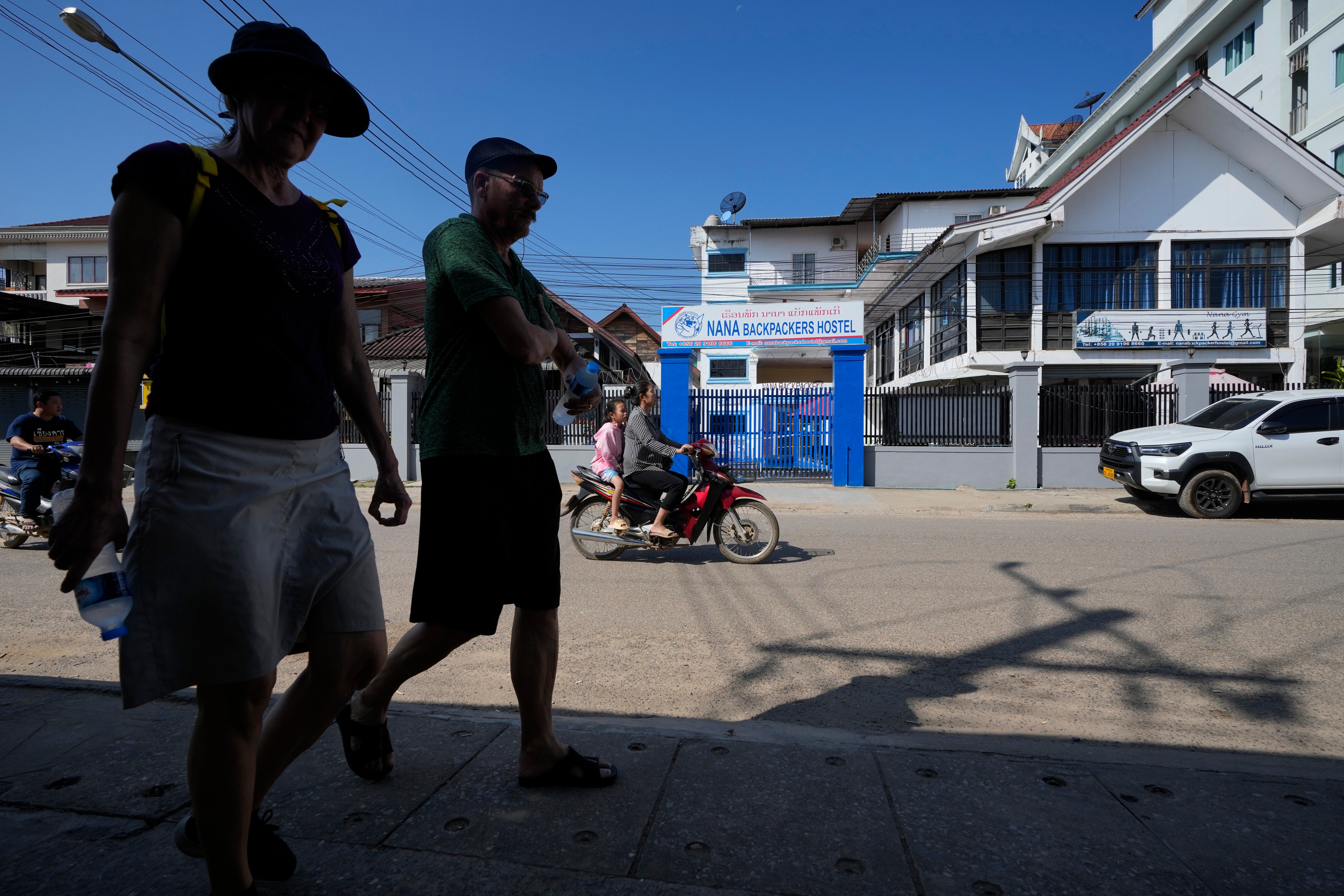 Foreign tourists walk past the closed Nana Backpackers hostel in Vang Vieng (Anupam Nath/AP)