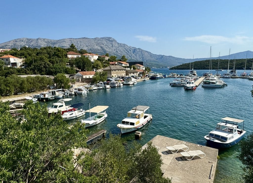 View over a small marina with boats in the bright turquoise water, mountains rising on the mainland in the background.