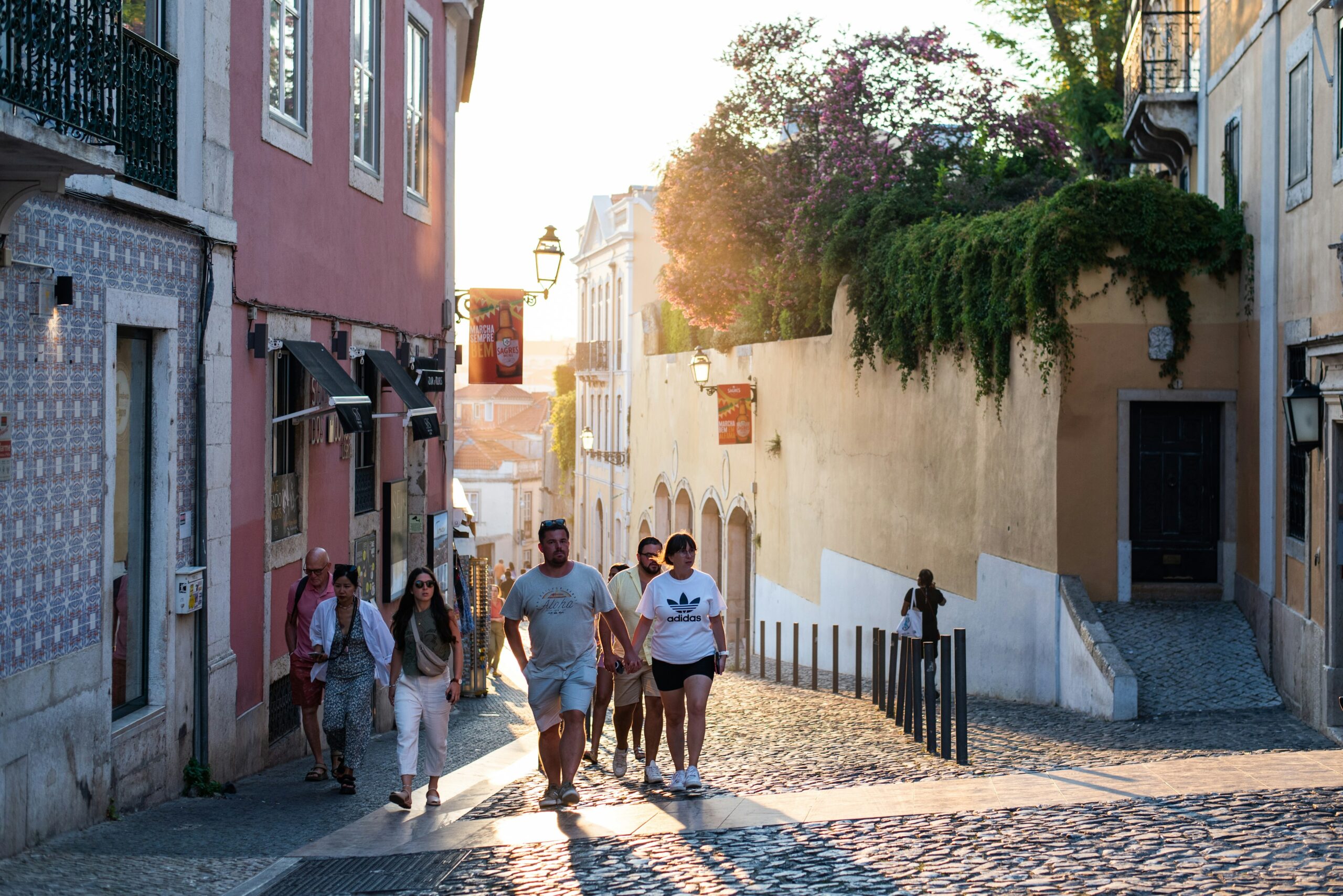 A group of people, including a couple holding hands, walk up a hill in Portugal with the sun setting behind them.