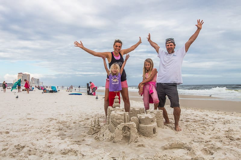 family posing in front of sand castle