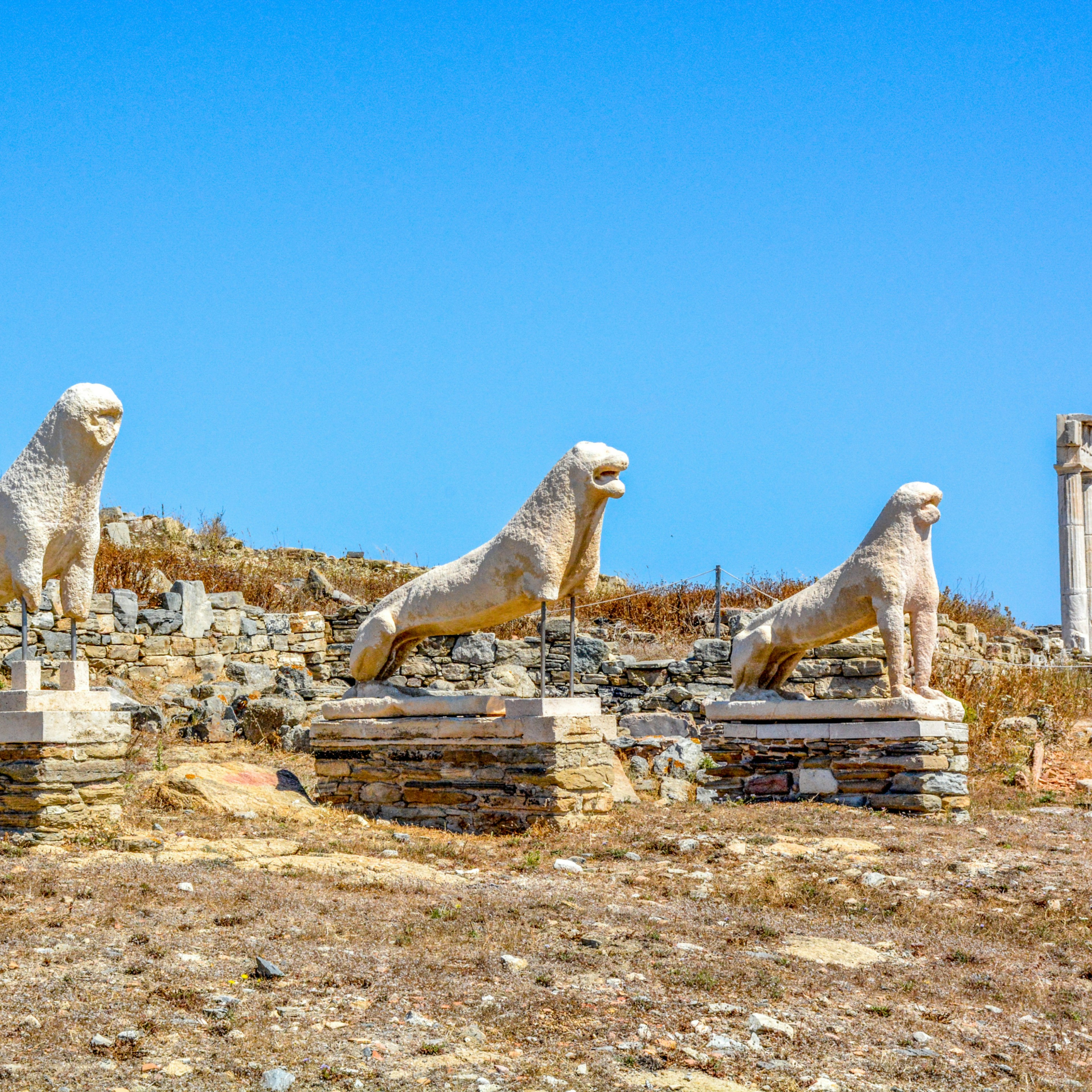 An ancient statue of a lion on a platform with a blue sky in the background.
