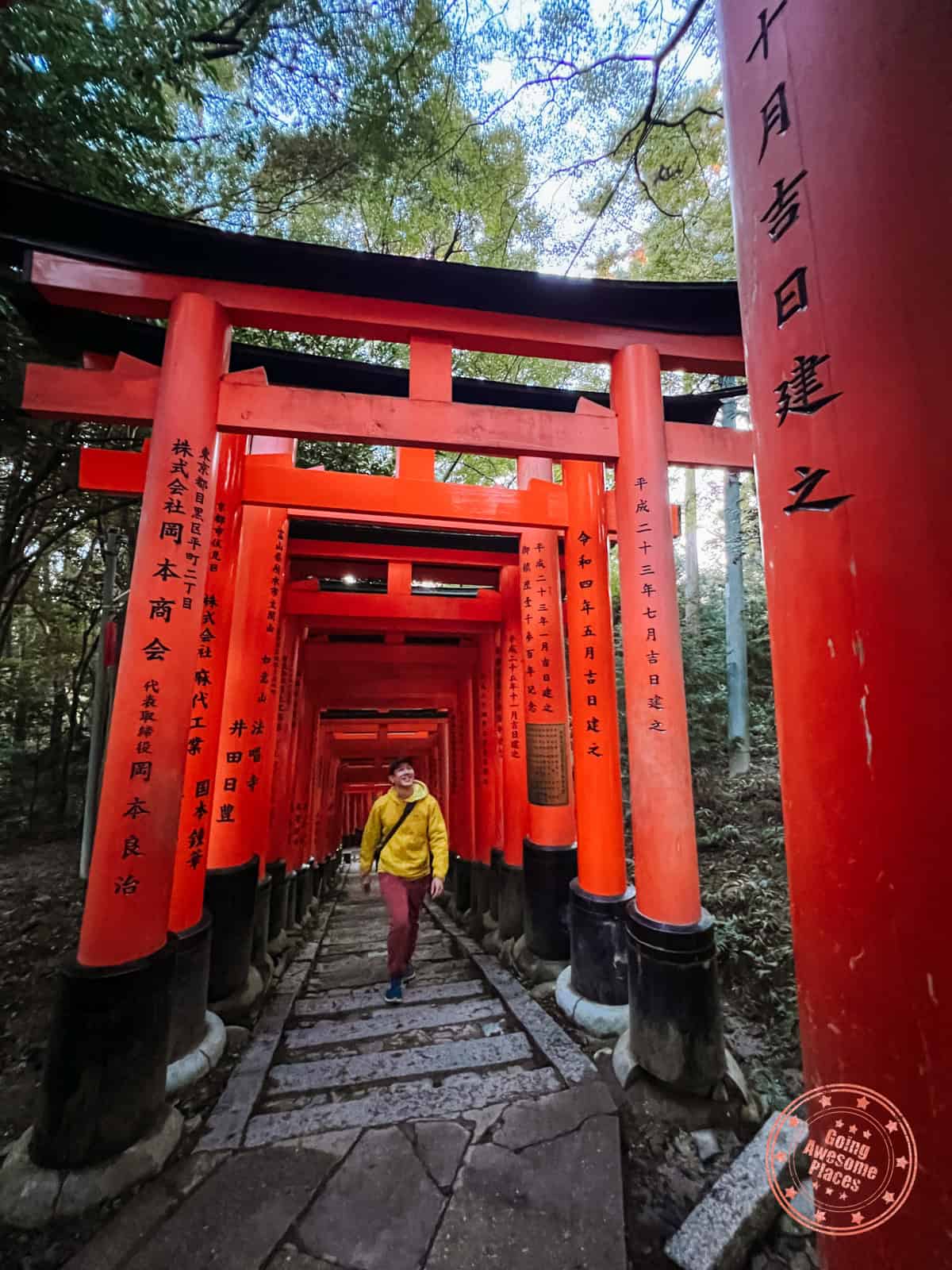 man with yellow jacket walking through red torii gates at fushimi inari shrine in kyoto