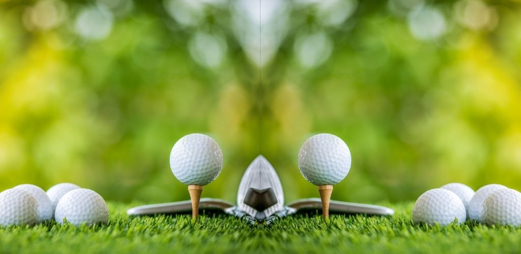 mirror image of golf ball on tee ready to practice, more golf balls on lawn to side of tee