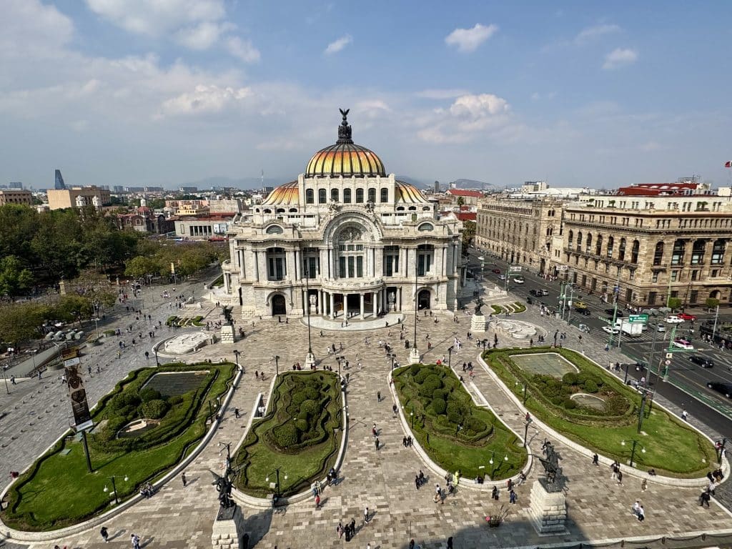The beautiful art deco palace of Bellas arts in Mexico City, with a bright yellow glass roof and small grassy parks in front.