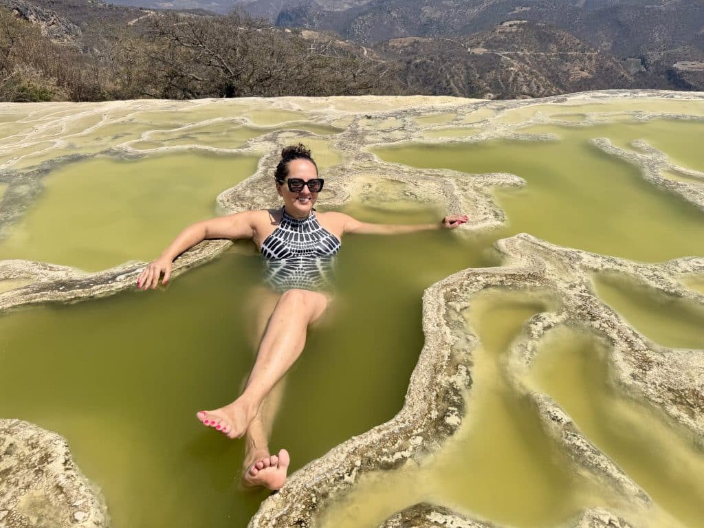 Kate lying in a green limestone pool overlooking a cliff's edge in Mexico.
