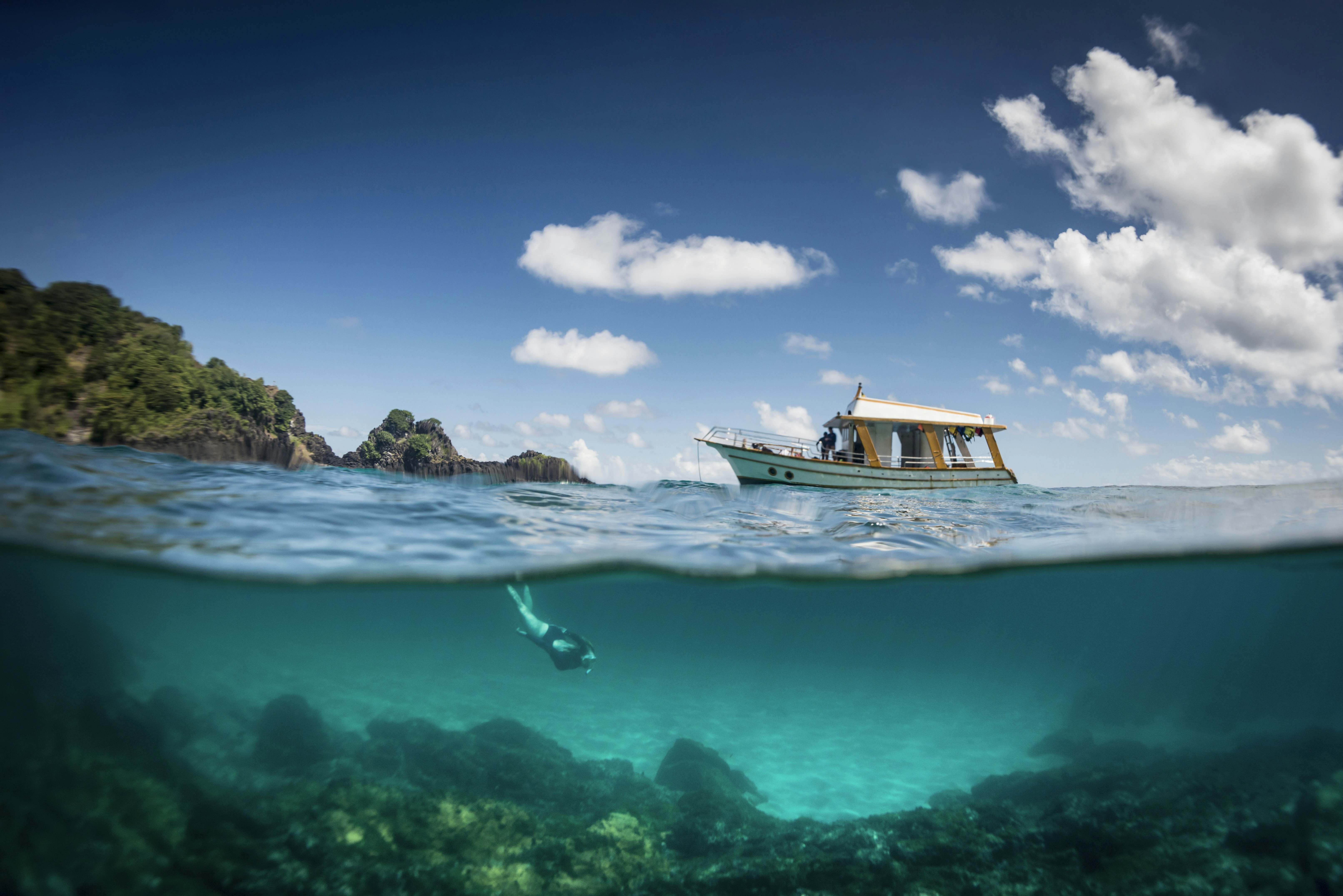 A woman snorkels underwater while a small tour boat moors nearby