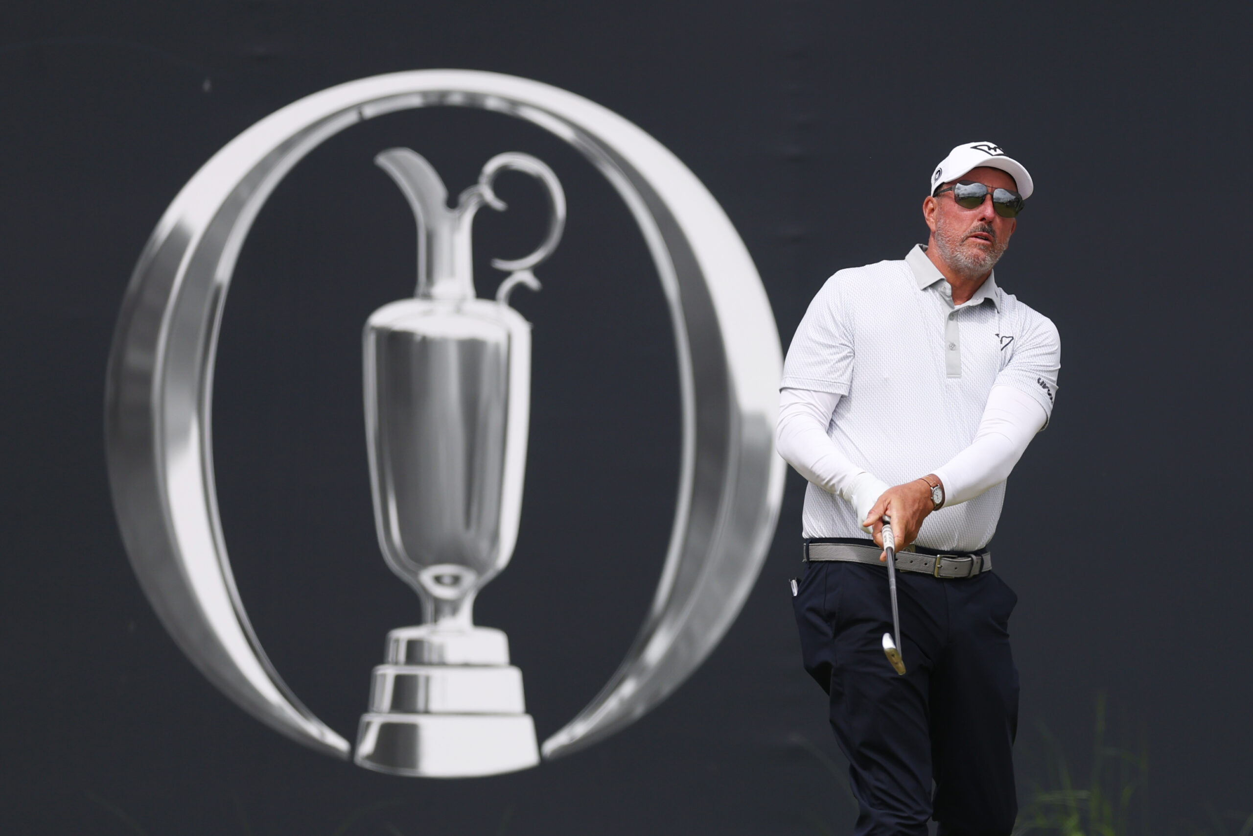 Phil Mickelson hits a shot in front of an Open Championship banner