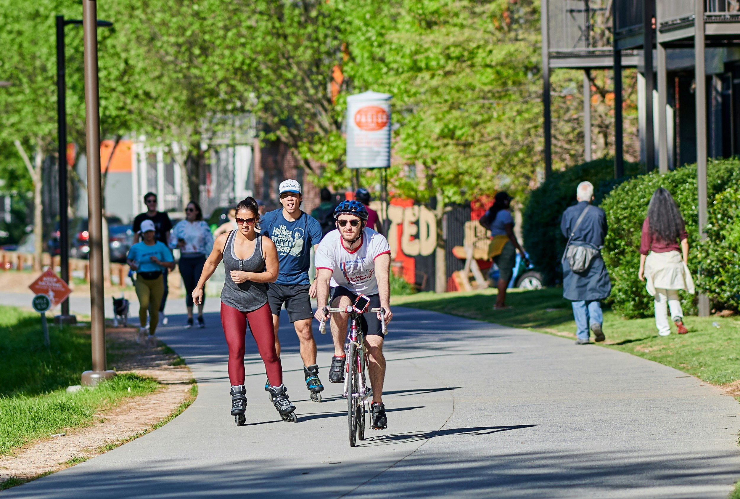 Many different people are cycling, rollerblading and walking along a stretch of the Atlanta Beltline on a sunny day