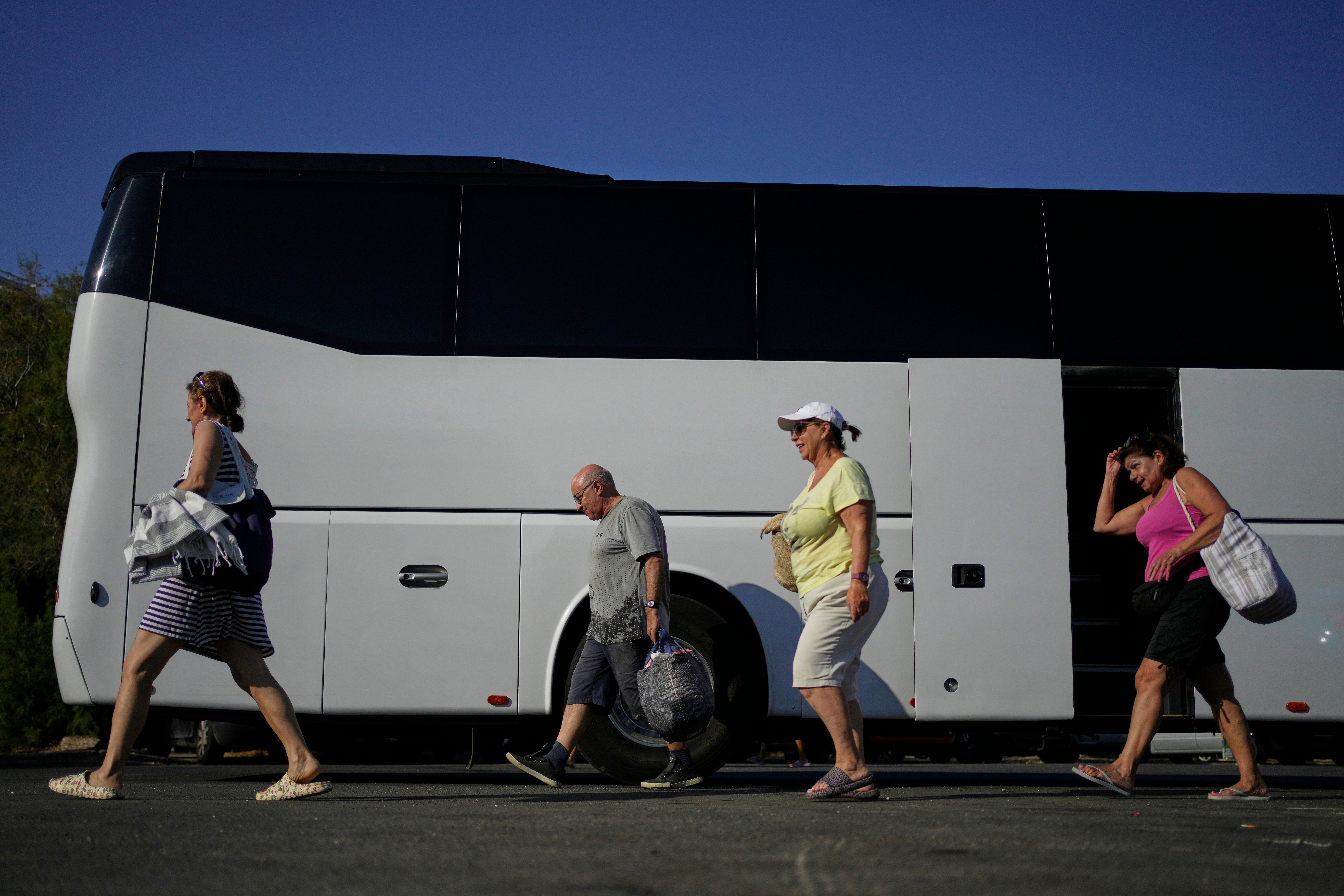 People arrive by bus at Avlaki beach about 42 kilometers (26 miles) east of Athens, Greece, Wednesday, Aug. 19, 2025. (AP Photo/Thanassis Stavrakis)