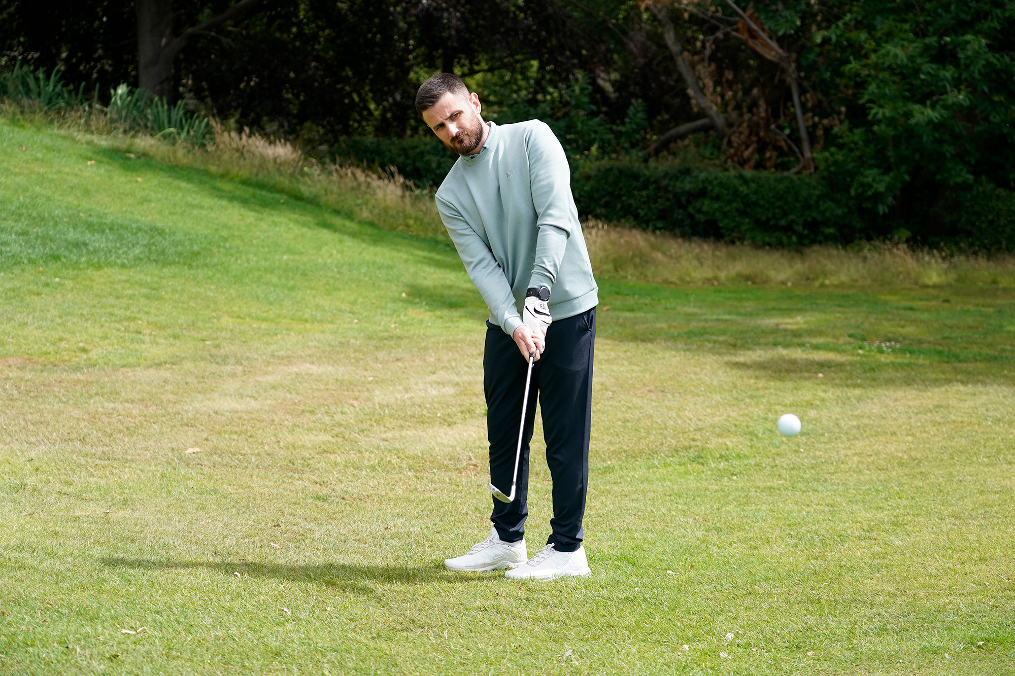 Baz Plummer hitting a chip shot from just off the green, with the ball in motion travelling towards the putting surface