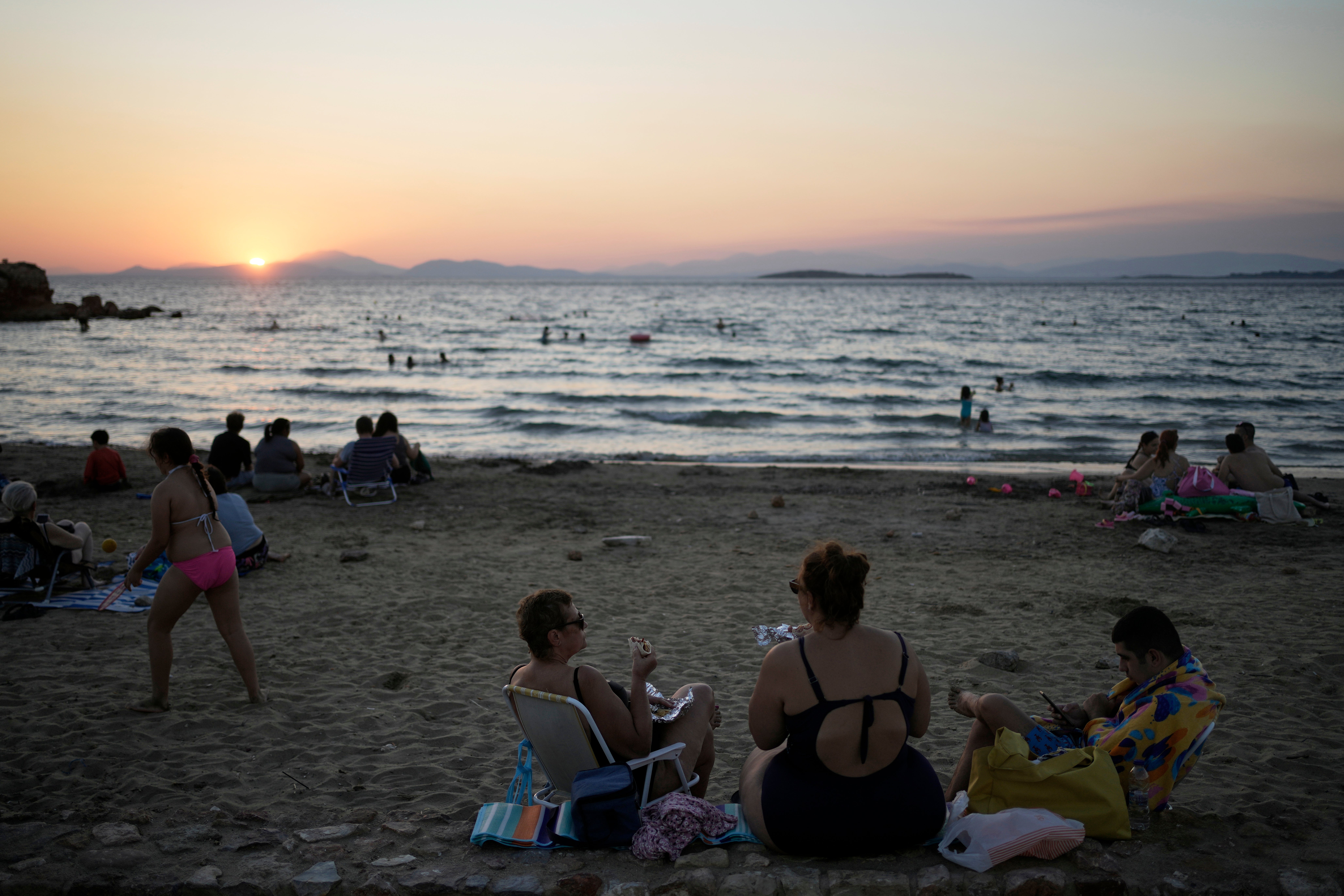 People gather at Kavouri beach as the sun sets in southern Athens, Greece, Monday, Aug. 11, 2025. (AP Photo/Thanassis Stavrakis)
